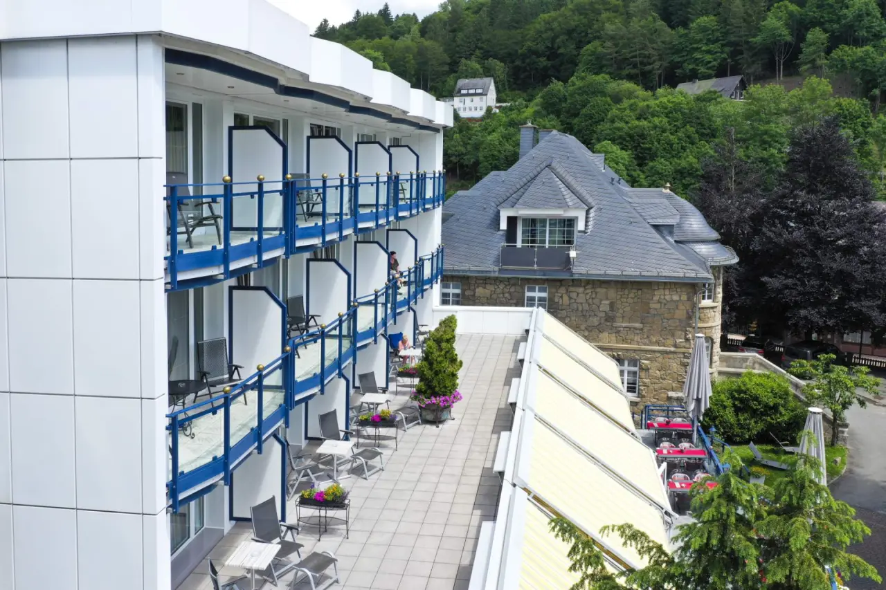Aussenansicht des Rüters Parkhotel mit modernen Balkonen, Terrasse und traditionellem Gebäude im Grünen.