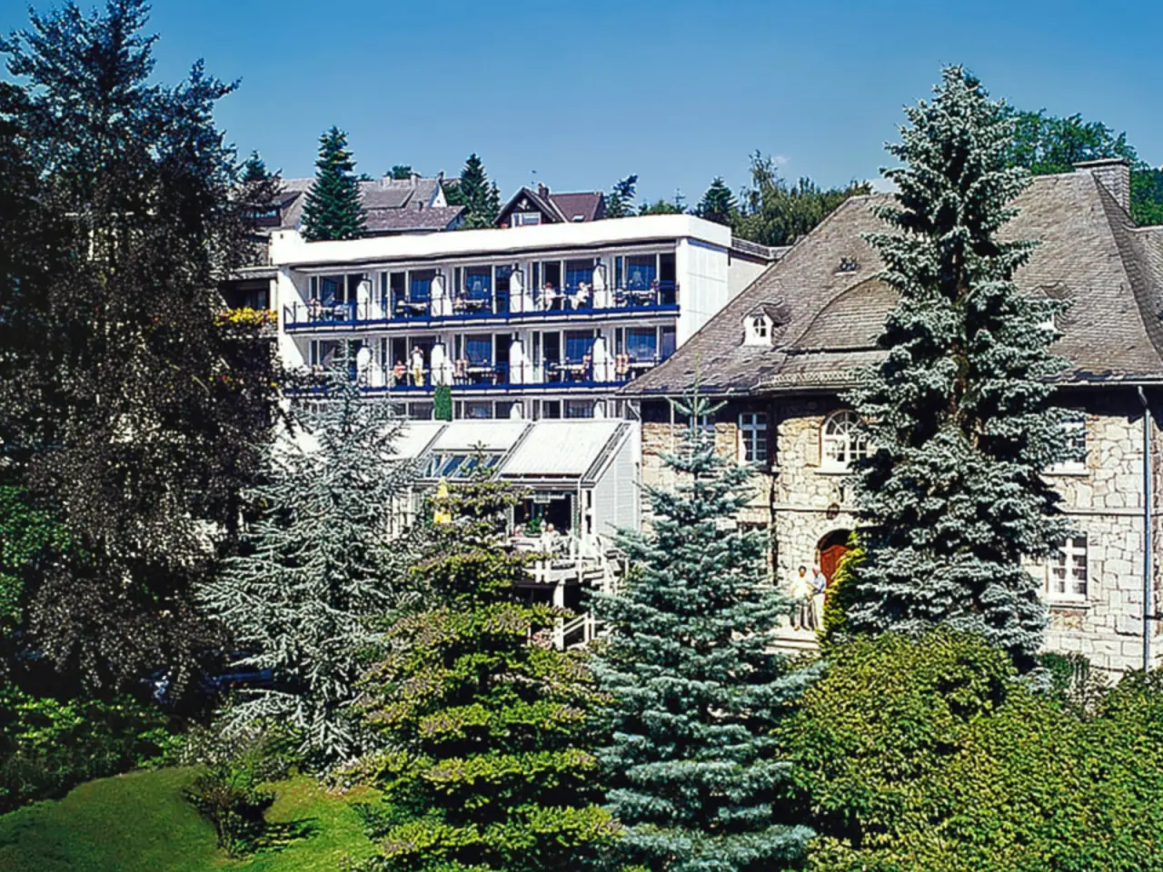 Aussenansicht des Rüters Parkhotel mit traditionellem Steinbau und modernem Anbau, umgeben von grünen Bäumen und Garten.