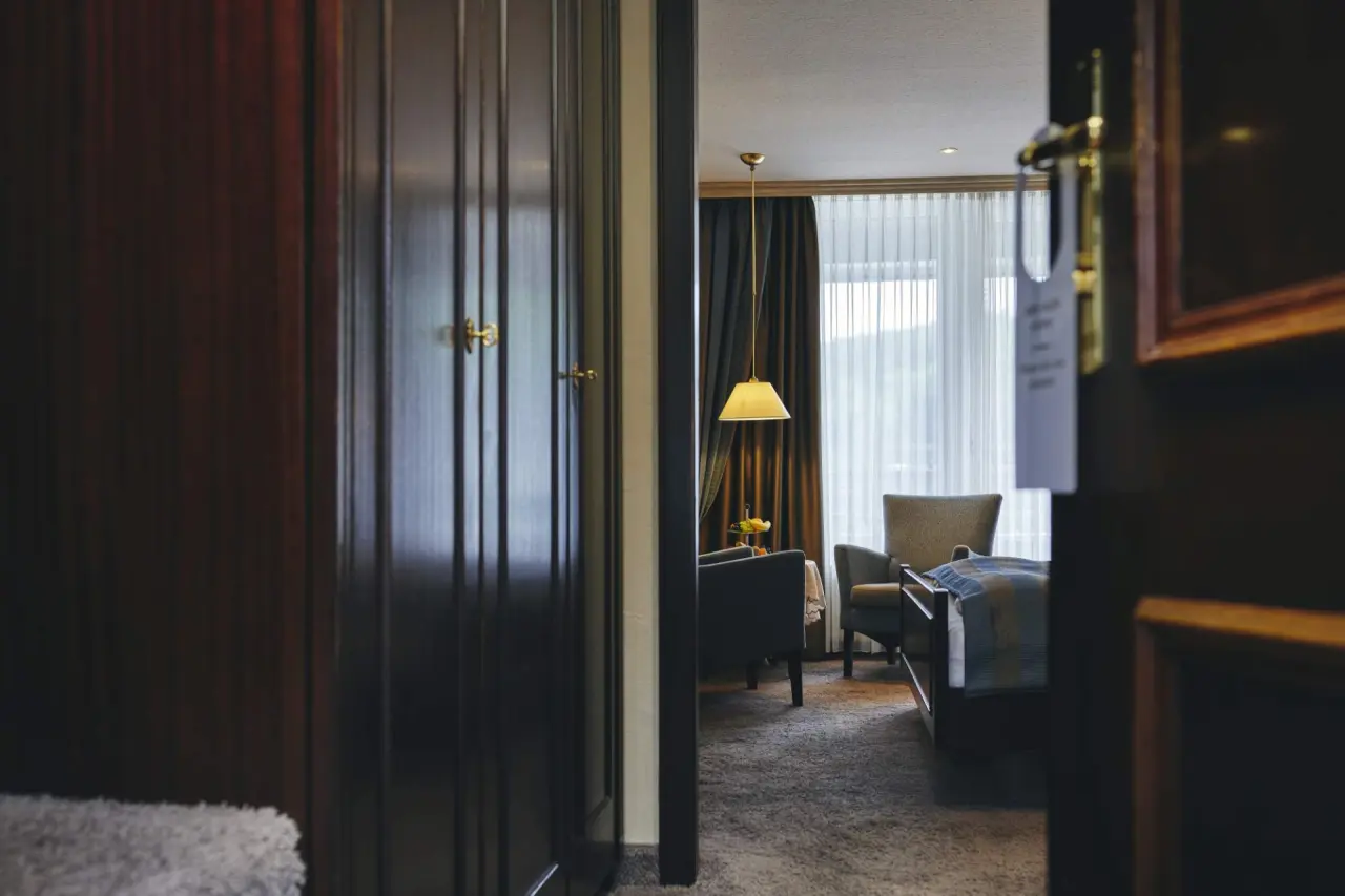 Gemütliches Hotelzimmer im Rüters Parkhotel mit bequemen Sesseln, Bett und Blick ins Grüne durch das Fenster.