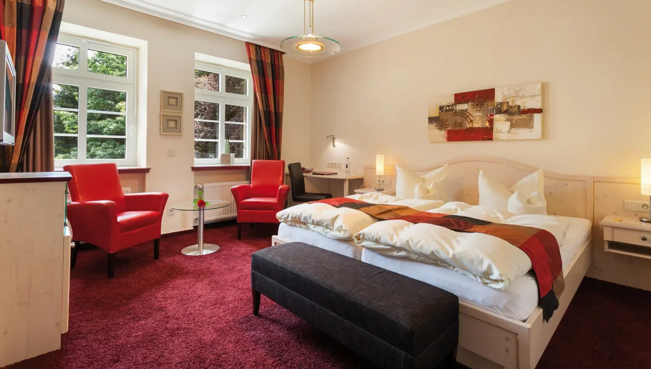 Komfortables Hotelzimmer mit Doppelbett, roten Sesseln und Schreibtisch im Rüters Parkhotel.