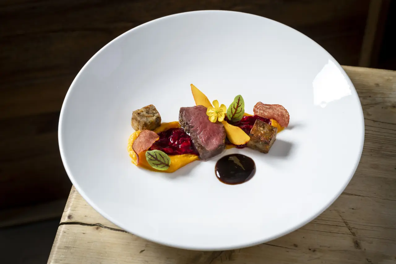Exquisit angerichtetes Gericht mit Fleisch und Beilagen im Restaurant des Hubertus Mountain Refugio Allgäu.
