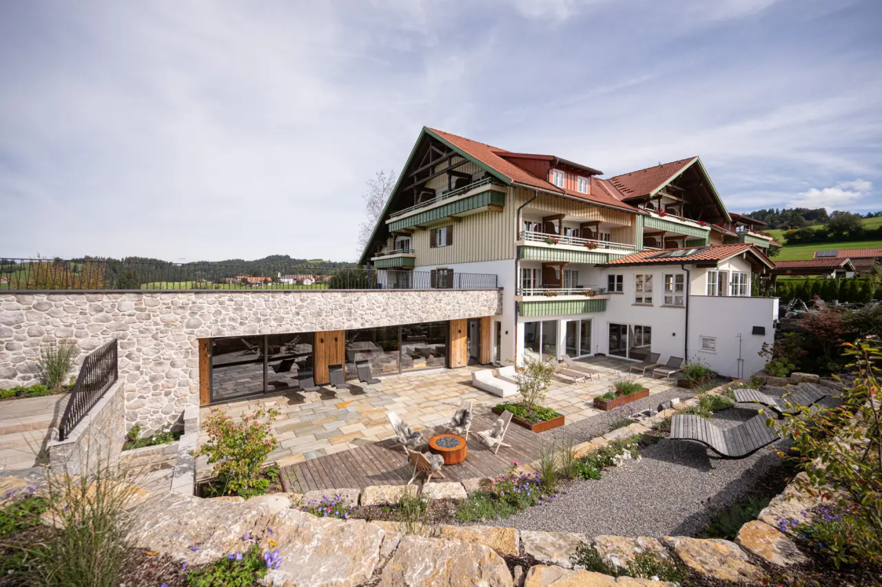 Aussenansicht des Hotel Johanneshof mit traditioneller Architektur, moderner Steinfassade und einladender Terrasse mit Feuerstelle und Lounge-Möbeln.