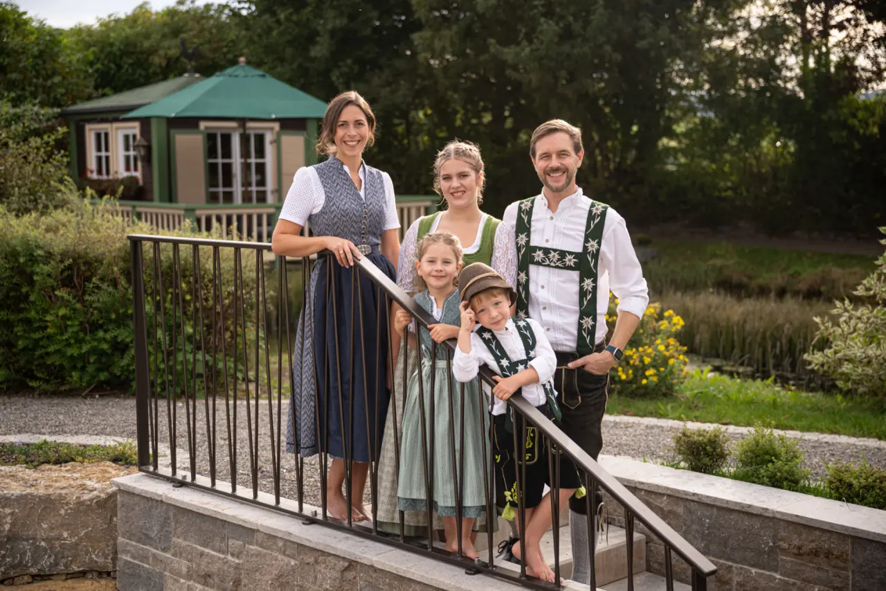 Gastgeberfamilie des Hotel Johanneshof in Tracht im grünen Hotelgarten mit historischem Pavillon.