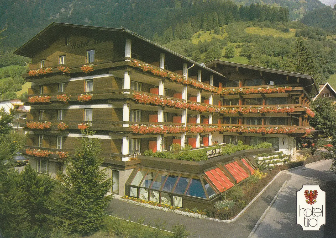 Aussenansicht des Impuls Hotel Tirol im alpinen Stil mit blumengeschmückten Balkonen und Poolbereich vor grüner Bergkulisse.