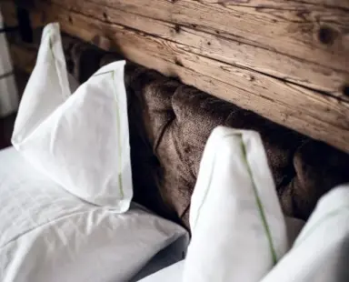 Nahaufnahme eines gemütlichen Bettes mit Holzkopfteil und weißen Kissen im Hotel Gotthard Lech.