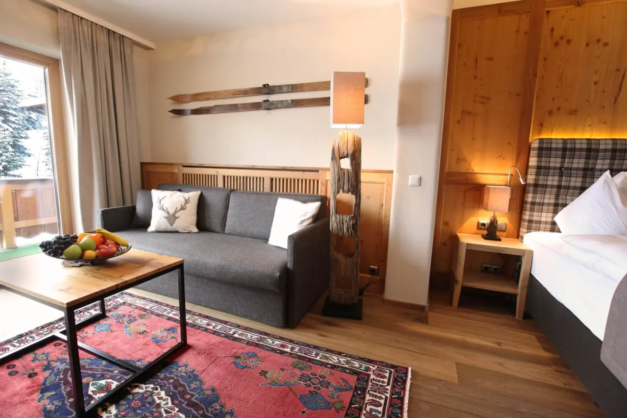 Gemütliches Hotelzimmer im alpinen Stil mit Sofa, Bett und Balkonzugang im Hotel Gotthard Lech.