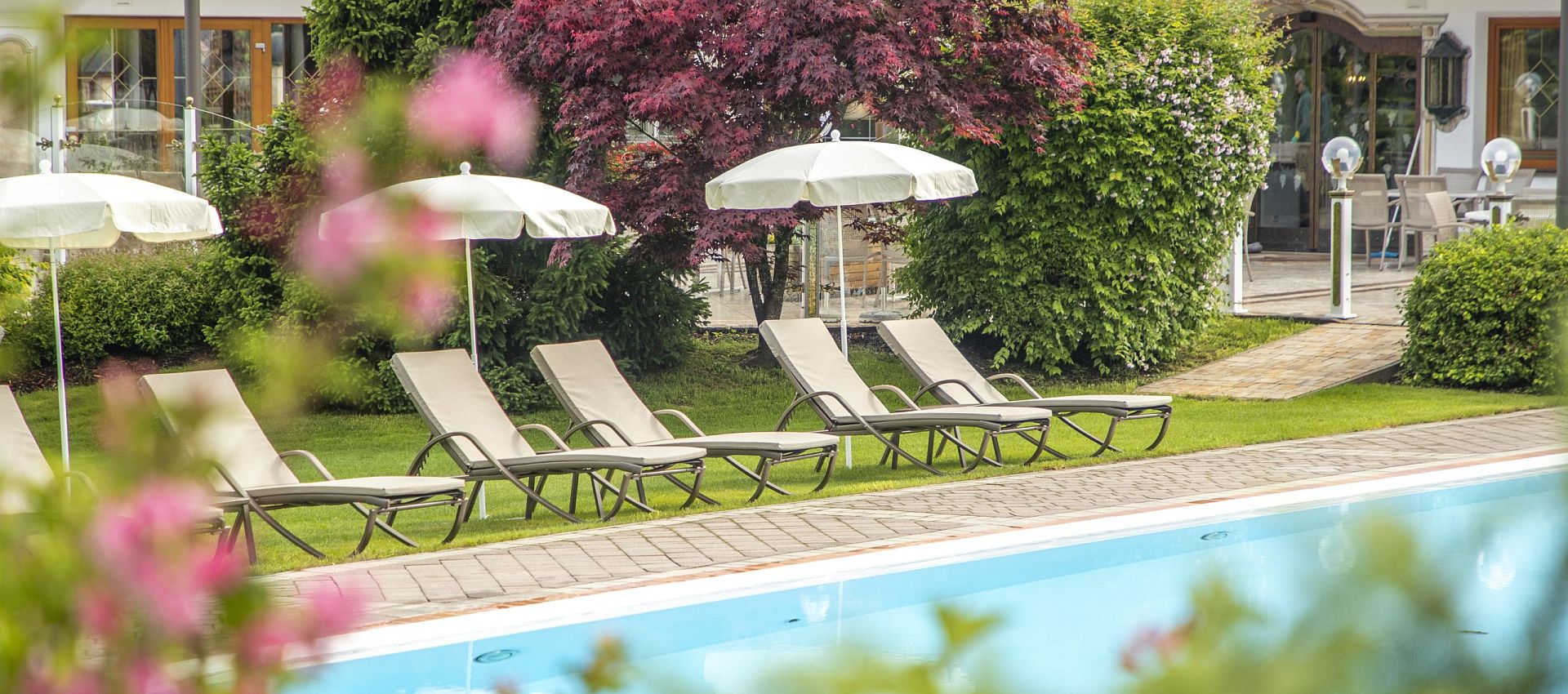 Hotel Der Lärchenhof in Erpfendorf – Außenpool mit Liegen und grüner Gartenanlage | Wellnesshotel Tirol