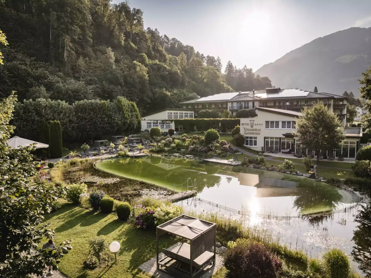 Naturschwimmteich und Hotel Vitalquelle Montafon umgeben von grünen Bergen im Montafon.
