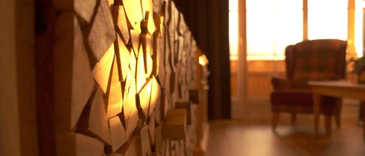 Dekorative Holzwand mit warmem Licht und unscharfem Sessel im Hintergrund im Hotel Zum Ritter.