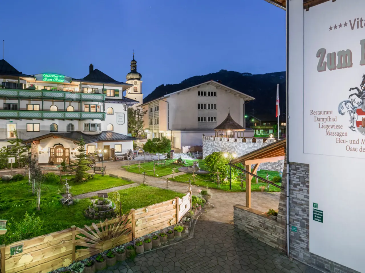 Abendliche Aussenansicht des Hotel Zum Ritter mit beleuchteter Fassade, idyllischem Garten und Hinweisen auf den Wellnessbereich.