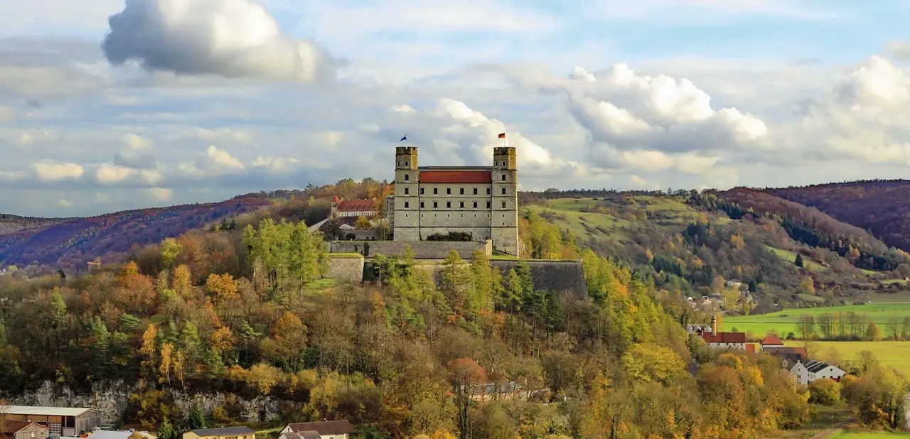 Majestätisches Wellnesshotel Schönblick, ein schlossartiges Gebäude auf einem bewaldeten Hügel, eingebettet in herbstliche Landschaft.