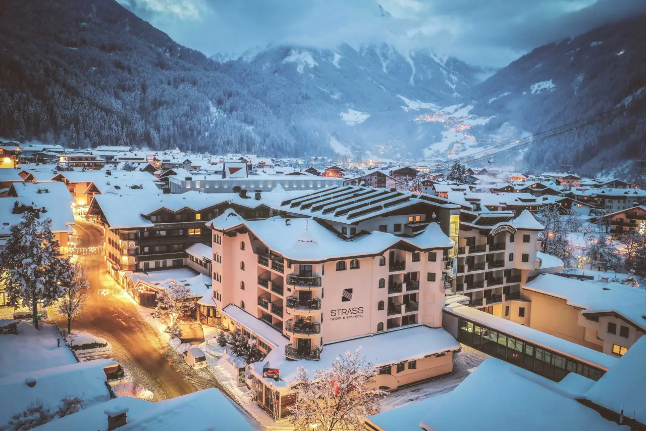 Winterliche Aussenansicht des Sport & Spa Hotel Strass in Mayrhofen bei Dämmerung, umgeben von verschneiten Bergen.