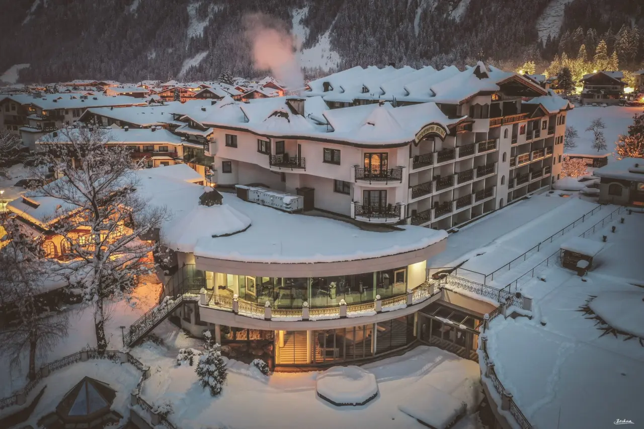Sport & Spa Hotel Strass im Winter: Beleuchtetes Hotelgebäude und verschneite Dächer in den Alpen bei Nacht.