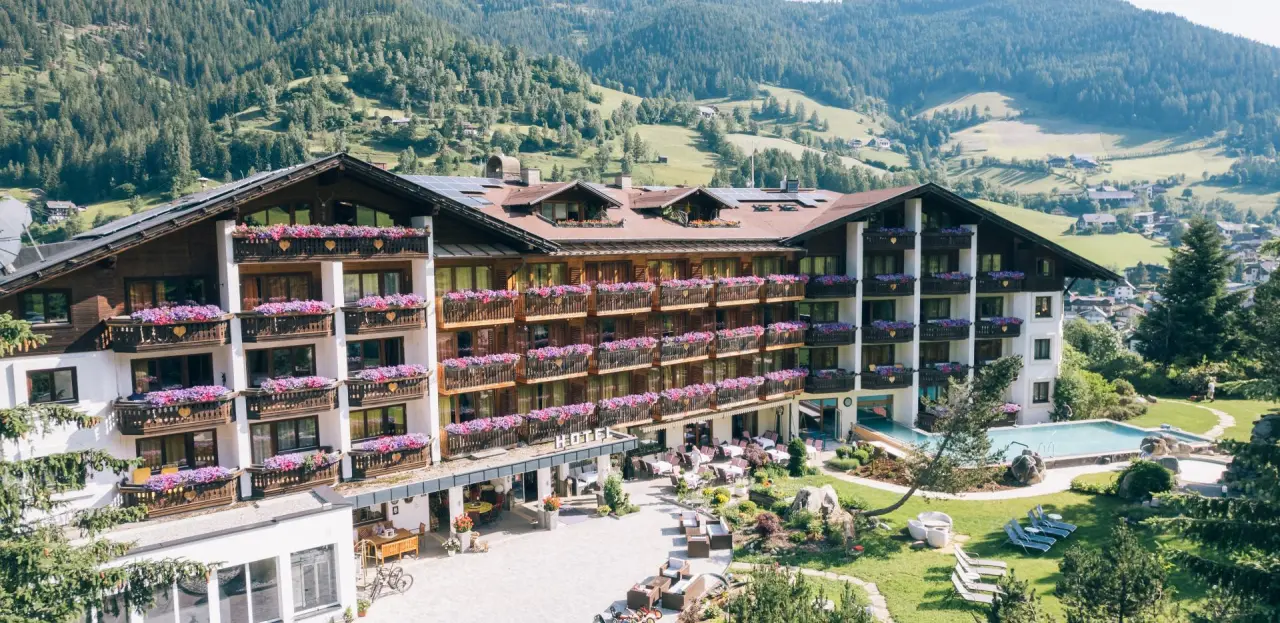 Panoramablick auf das Hotel Der Kirchheimerhof mit blühenden Balkonen, Aussenpool und grüner Berglandschaft.
