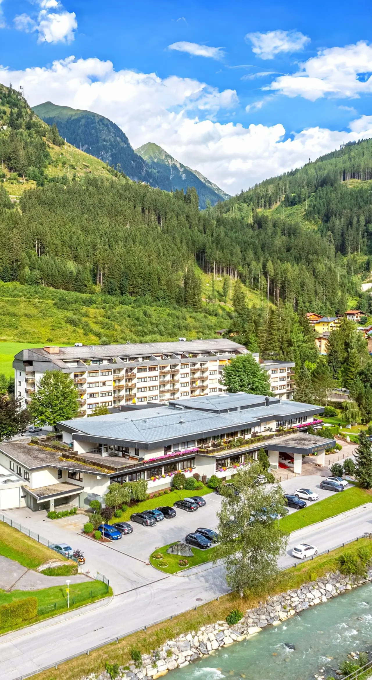 Luftaufnahme des EUROPÄISCHER HOF Aktivhotel & Spa in den Alpen, umgeben von grünen Wäldern und einem Fluss.