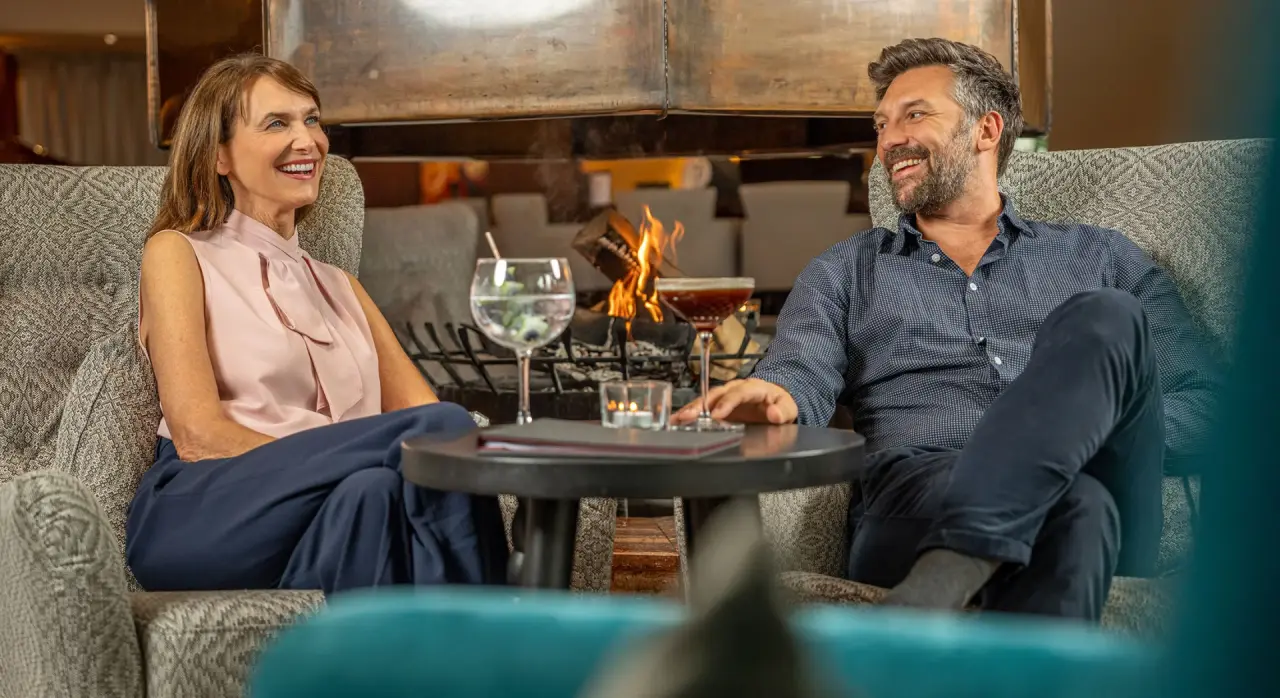 Glückliches Paar entspannt am Kamin in der gemütlichen Lobby des EUROPÄISCHER HOF Aktivhotel & Spa.